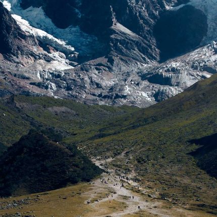 Hikers walking on a mountain trail toward the rocky base and glaciers of Mount Salkantay.