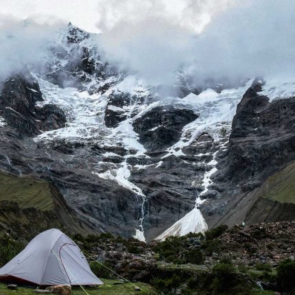 Camping tent pitched in front of the snow-capped Salkantay mountain partially covered by clouds.